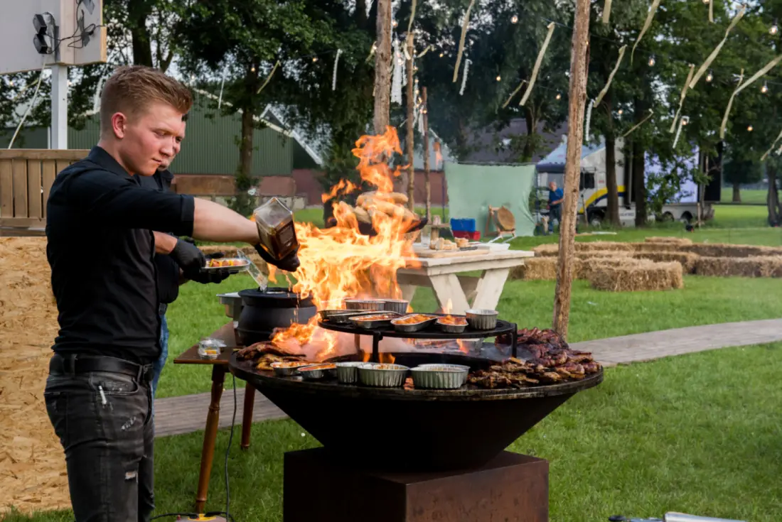 Een kok van B&G Catering aan het werk bij de vuurschaal, buiten op een feest